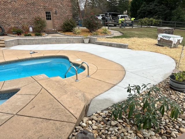 Backyard pool with curved concrete deck and rock landscaping beside a brick house