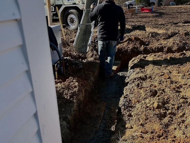 Person carrying a rolled material in a muddy trench beside a white truck at a construction site