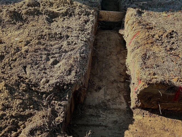 Mud-filled trench between two rough earth walls with a narrow gap at the far end.