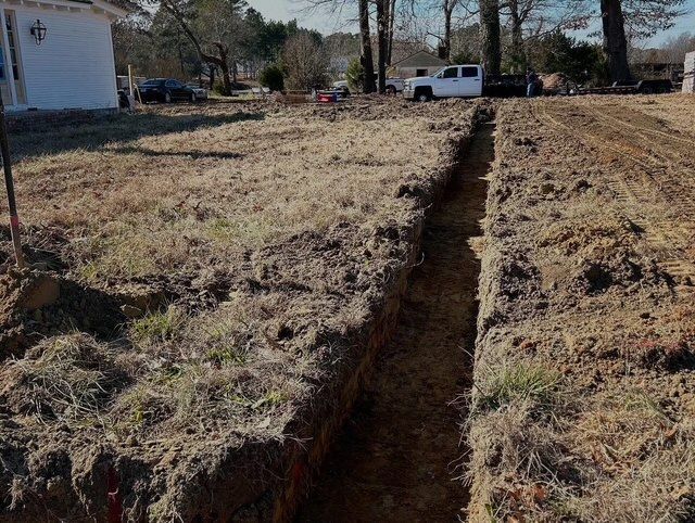 Deep trench cut through a grassy yard beside a house, with a white truck in the background.
