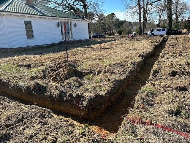 Trench dug through a grassy yard beside a white house, with exposed soil and a red marking line.