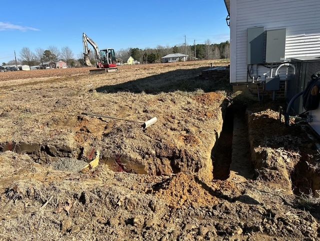 Excavator digging a trench beside a building on a sunny construction site