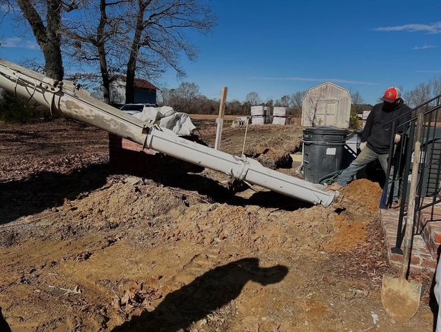 Collapsed utility pole over muddy roadside, with workers and equipment nearby under a clear sky