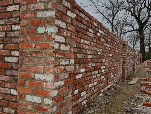 Partially built red-brick wall along a dirt path in a wooded area