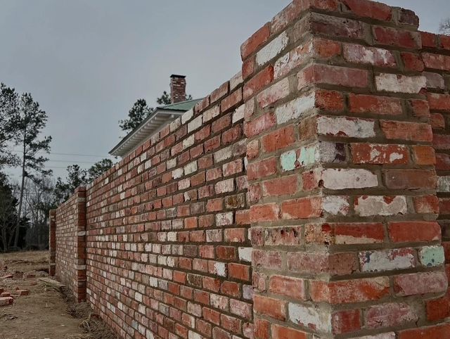 Long brick wall under construction outdoors, with trees in the background