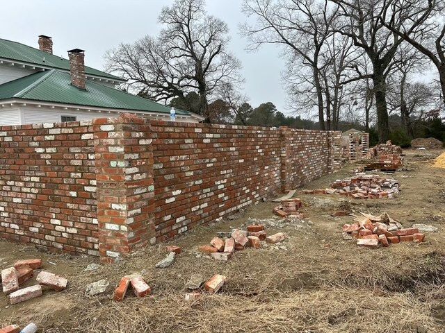 Partially demolished brick wall beside a green-roofed building, with scattered bricks on the ground.
