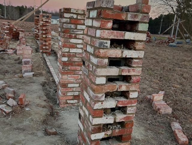 Stacked red bricks forming wall pillars at a construction site on bare ground