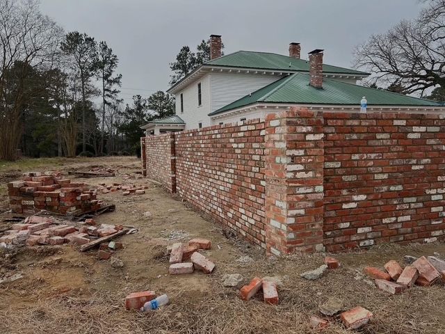 Partially built brick wall and scattered bricks beside a house under construction