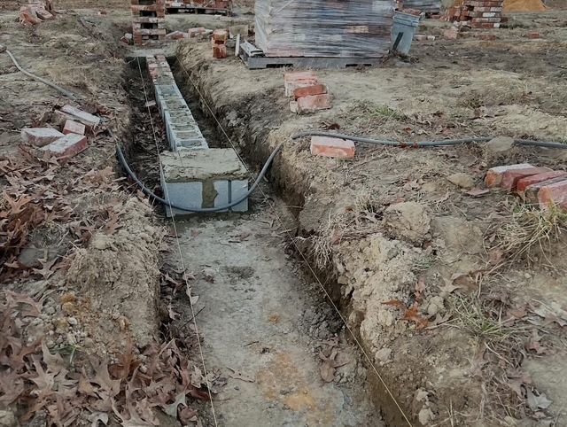 Construction trench with a narrow concrete channel and exposed bricks in a muddy, excavated area