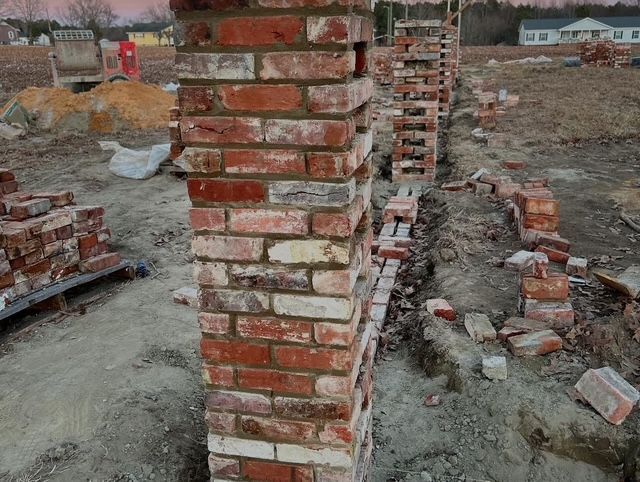 Partially built brick columns at a construction site with rubble and dirt ground