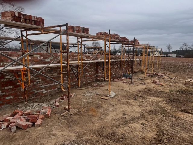 Scaffolded brick wall under construction on a barren site with piles of bricks and cloudy sky