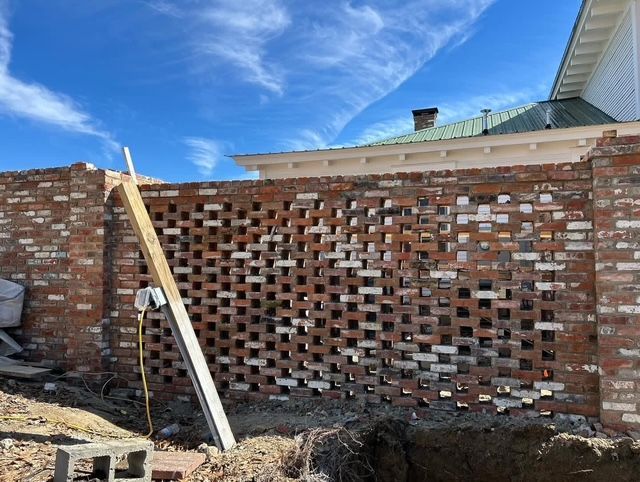 Partially built brick wall with a wooden support beam under a blue sky