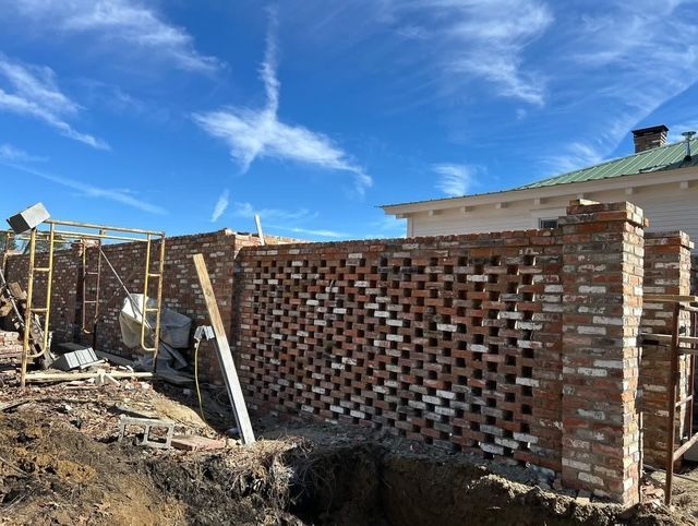 Brick wall under construction beside a dirt lot, with blue sky and wispy clouds overhead