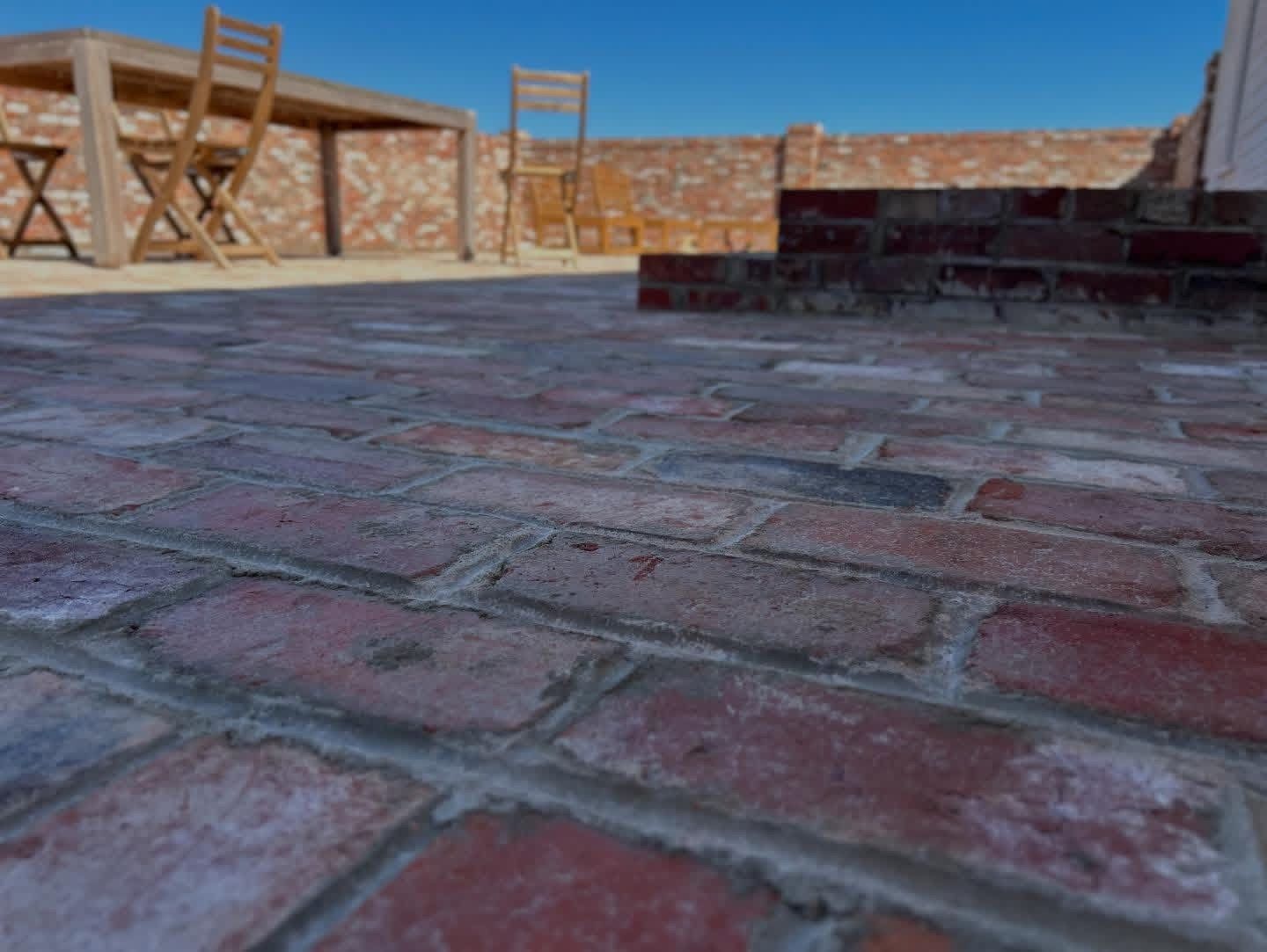 Low-angle view of a brick rooftop patio with chairs and a blue sky.