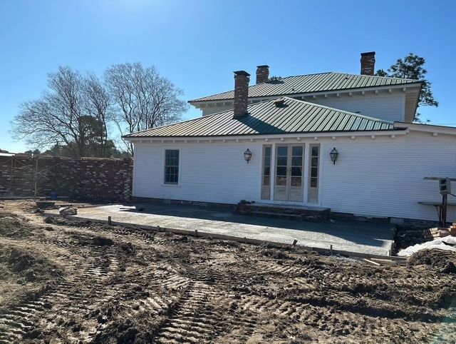 White house with double doors, chimneys, and unfinished dirt yard under a clear blue sky.