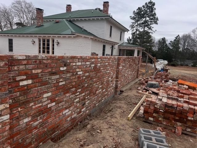 Brick wall under construction beside a white house on a muddy residential site