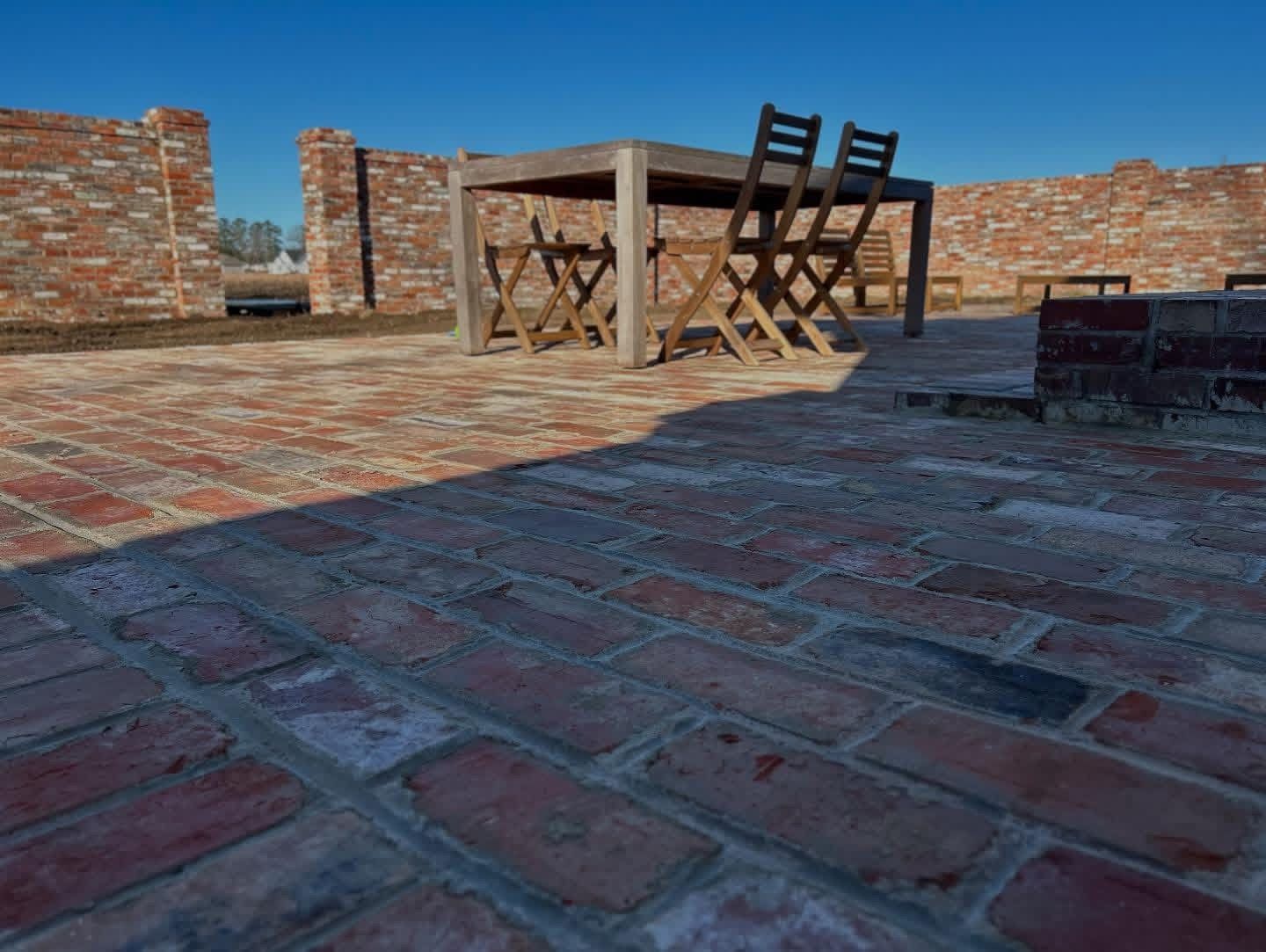 Brick patio with a wooden table and chairs against low brick walls under a blue sky