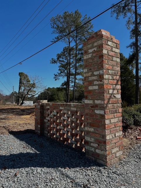 Brick pillar and lattice wall beside a gravel driveway under a blue sky.