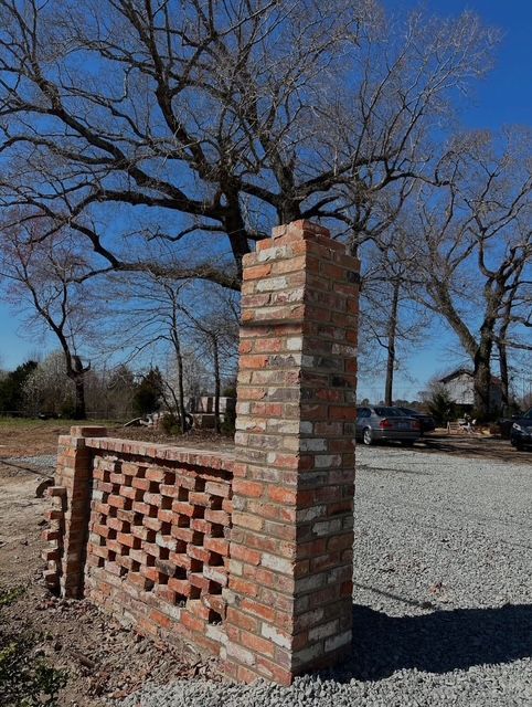 Brick sign structure with a lattice wall beside a gravel lot under a leafless tree and blue sky