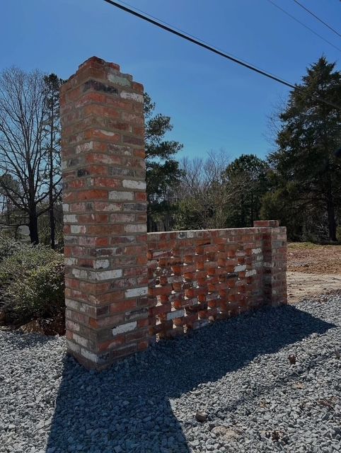 Partially built red brick wall with a chimney-like pillar outdoors under a blue sky