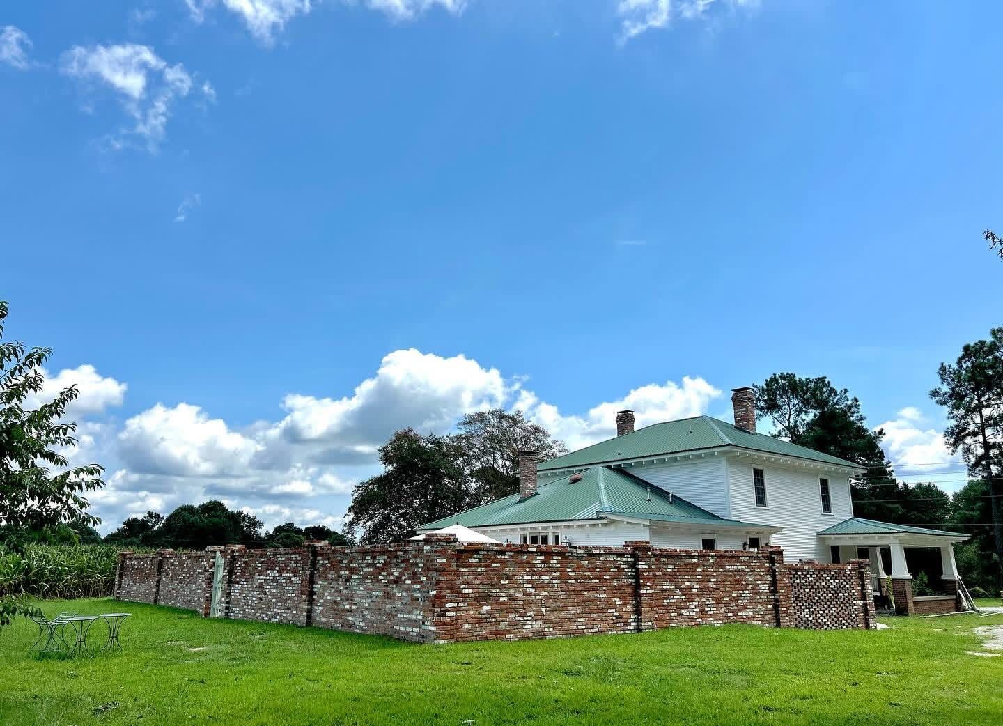 Old brick wall in front of a green-roofed building under a bright blue sky with clouds