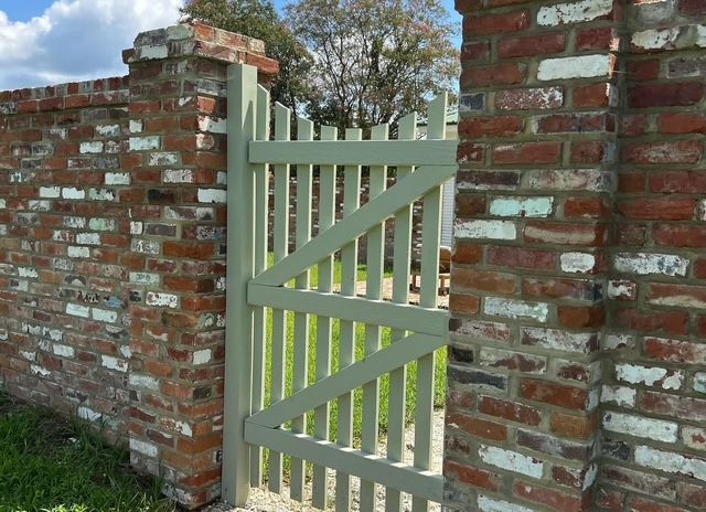 Light green wooden gate set in a red brick wall outdoors.
