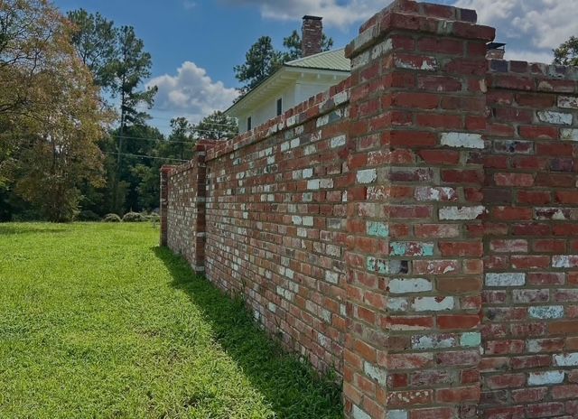 Brick wall with white mortar beside a grassy lawn and trees under a blue sky
