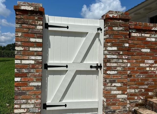 White wooden gate with black hinges between two brick pillars under a blue sky