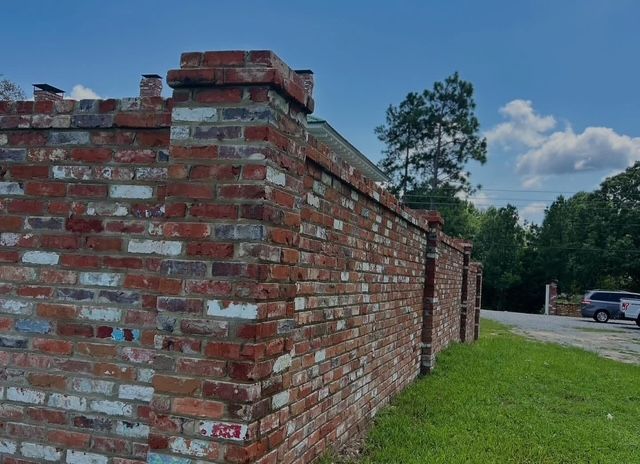 Brick wall beside a grassy roadside under a blue sky with clouds