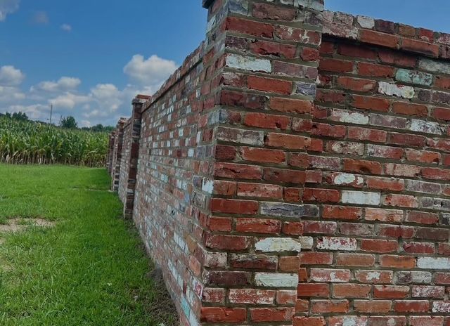A long brick wall under a blue sky, with green grass beside it.