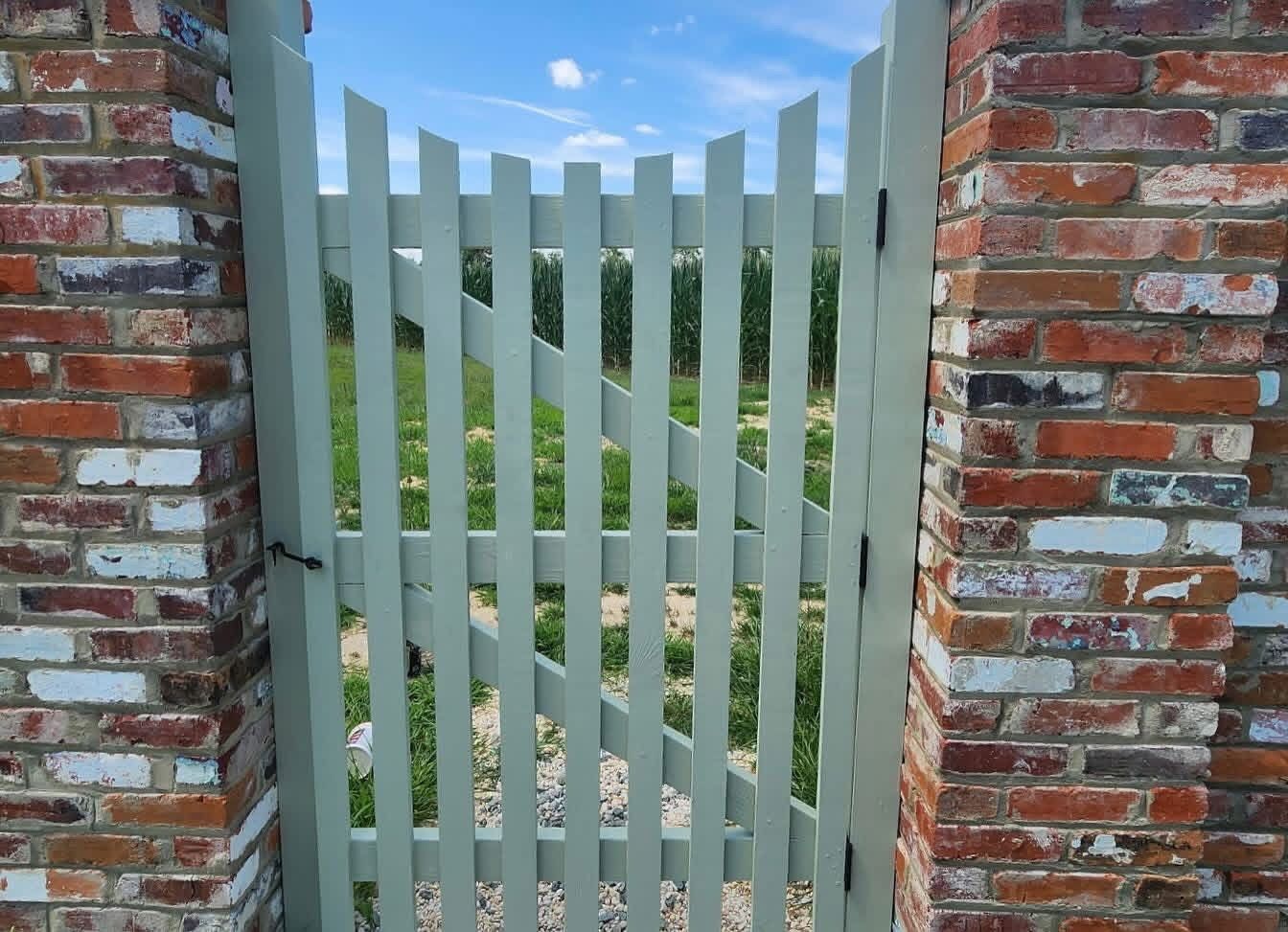 Light green wooden gate set in a red brick wall, opening to a grassy outdoor area.