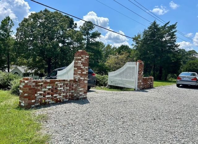Paver walkway beside a house leading to a driveway, with green lawn and parked white cars in the background
