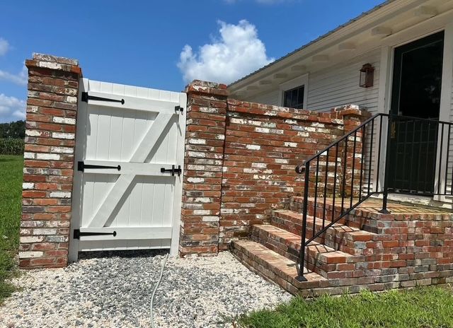 Brick wall and white gate beside house steps with black railing under blue sky