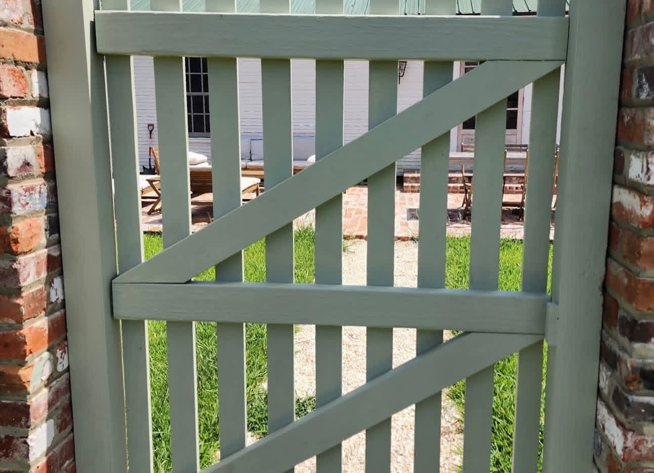 Closed pale green wooden gate with diagonal slats in front of a yard and stone pillars