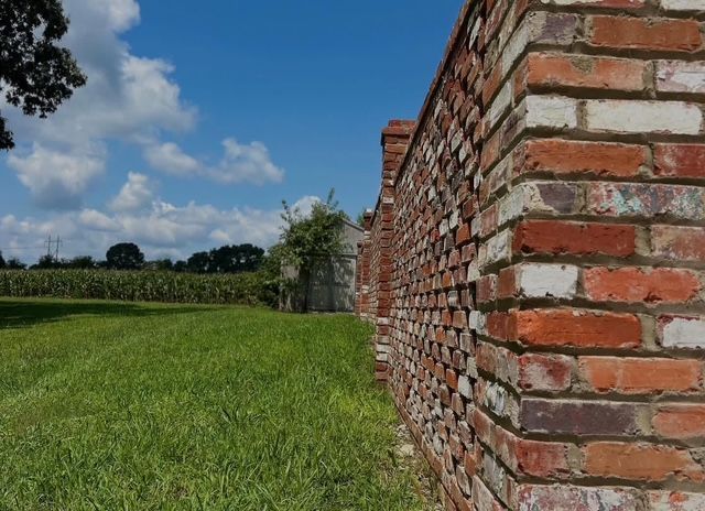 Brick wall beside a green field under a partly cloudy blue sky