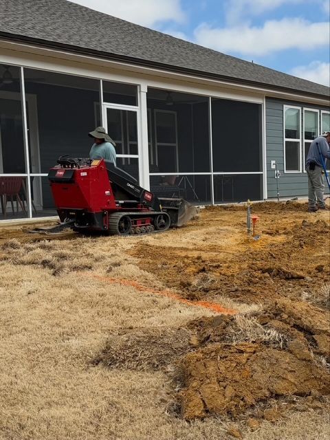 Workers using a red machine to level dirt beside a house under construction