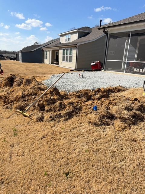Backyard patio under construction beside a house, with gravel, straw, and a screened porch