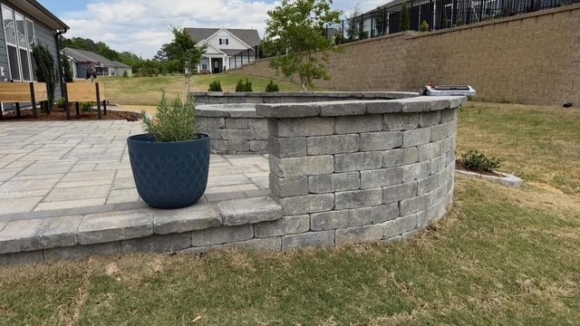 Stone patio with a blue planter beside a curved brick outdoor wall on a grassy lawn