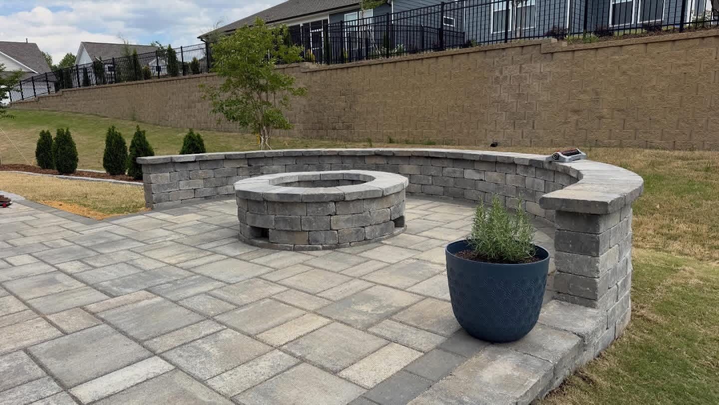 Stone patio with circular fire pit, curved bench wall, and blue planter in a landscaped courtyard.