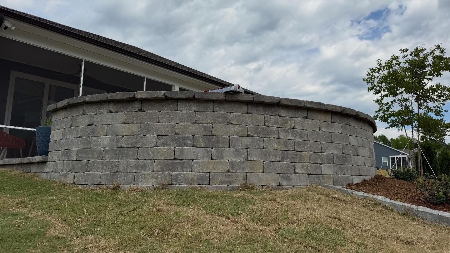 Curved gray stone retaining wall beside a house under a cloudy sky