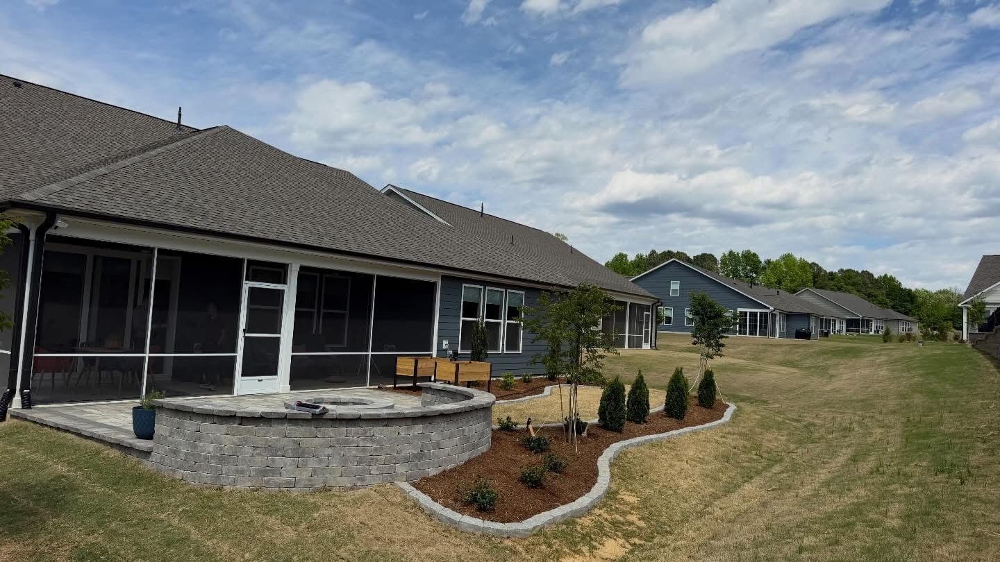 Suburban backyard patio with stone fire pit, sliding doors, and landscaped lawn under a cloudy sky