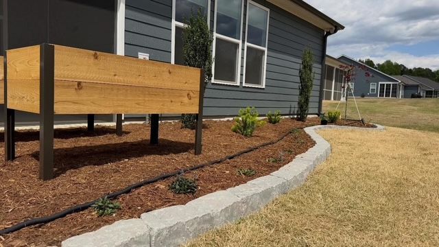 Wooden planter beside a house with a curved concrete border and landscaped mulch bed.