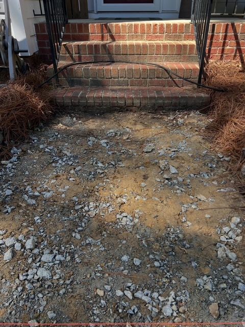 Rocky gravel path leading up to brick front steps and porch, with bare shrubs on both sides