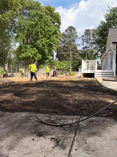Workers in neon shirts leveling soil beside a house and porch on a sunny day