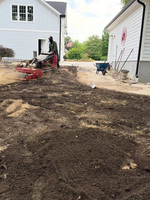 Worker using a red excavator to clear dirt beside white houses on a residential lot