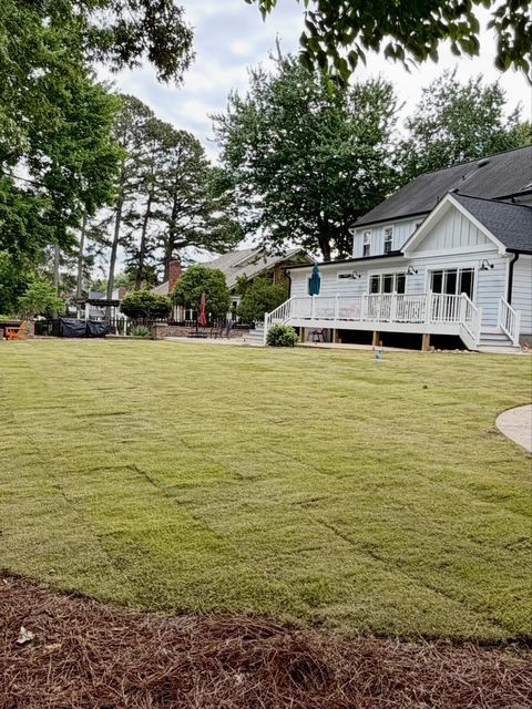 Backyard with freshly sodded lawn beside a white house with porch and trees