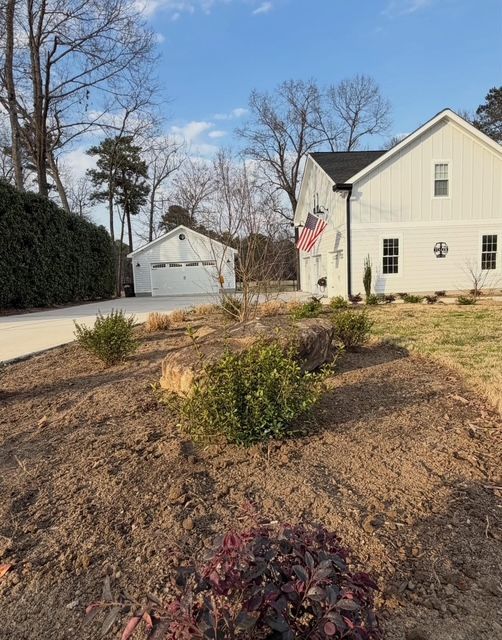 Front yard mulch beds with small shrubs beside a white house and driveway under a blue sky