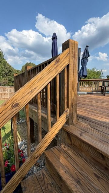 Wooden deck stairs and railing with closed blue patio umbrellas under a partly cloudy sky