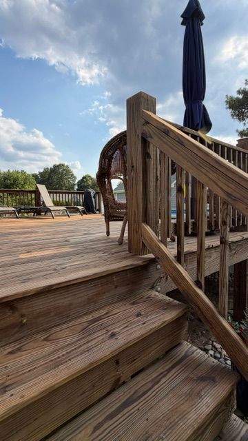 Wooden deck stairs with railing leading to an outdoor seating area with closed umbrella under a blue sky
