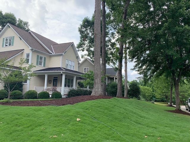 Suburban house with a covered porch, large trees, and a green lawn on a quiet street